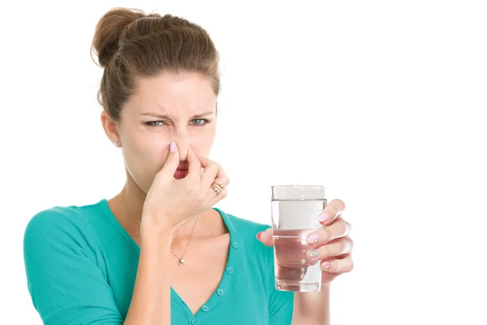 Woman holding her nose at a glass of water with an odor